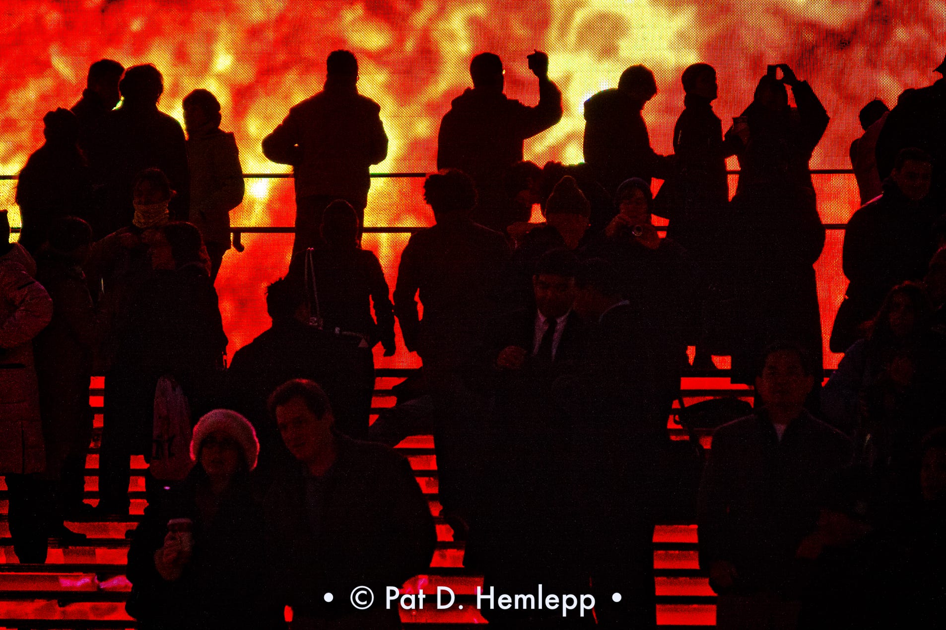 Visitors silhouetted against the flames of a video billboard atop the ruby red steps in Times Square, New York City.